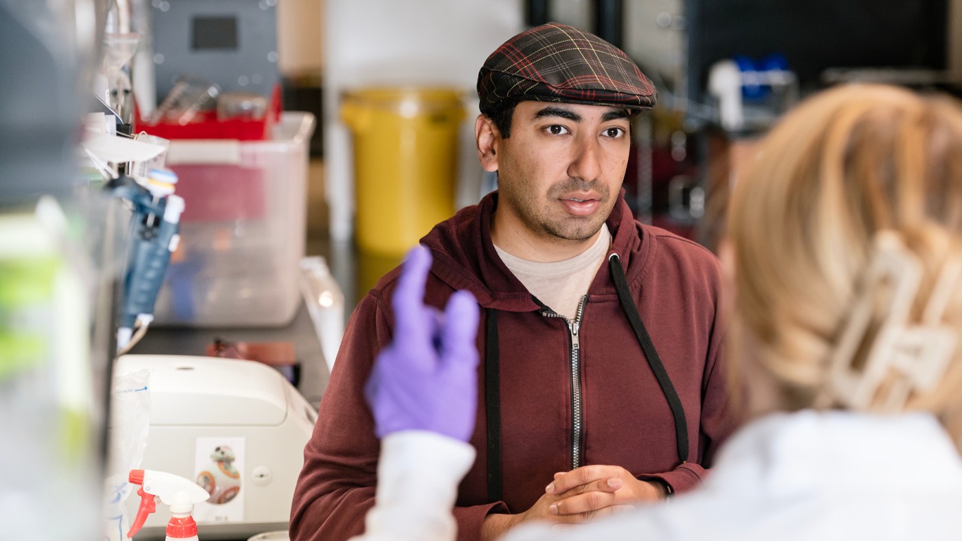Close up of Sukrit Silas working in the lab talking to someone.