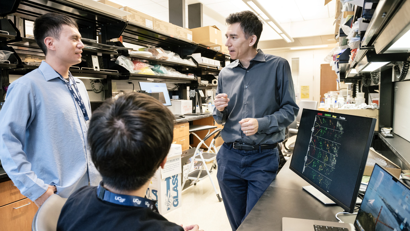 Ken Nakamura talking to two scientists by a computer in the lab at Gladstone Institutes