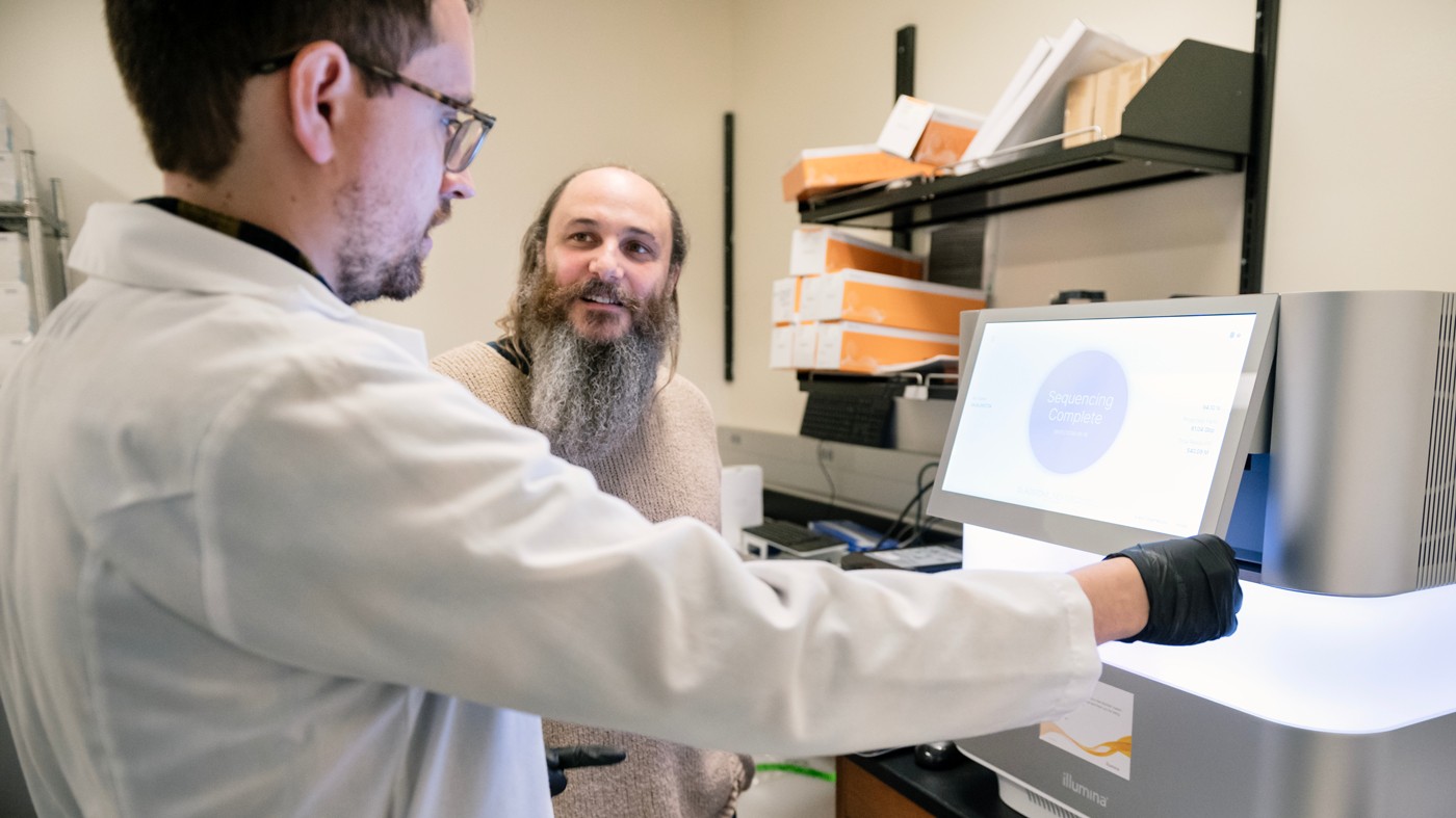 Seth Shipman talking to another scientist in front of scientific equipment at Gladstone Institutes